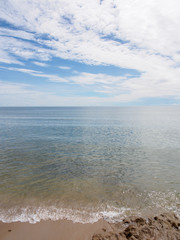 Wide angle view of waves breaking into a dark, smooth sandy beach with a beautiful cloud formation on a sunny day. Hua Hin, Thailand. Travel and nature concept.