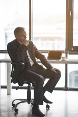 Full length side view pensive old businessman having job with digital device at table. Wistful employer in office concept