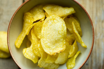 Isolated salted potato chips in a little bowl on the wooden background