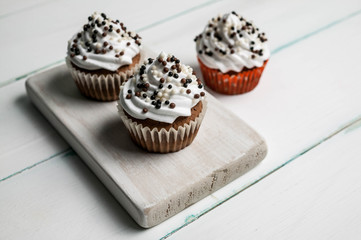Vanilla cupcakes with butter cream with chocolate topping on a wooden chopping board on a light background