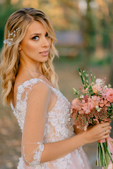 young beautiful bride holding a wedding bouquet and looking at the camera on a nature background