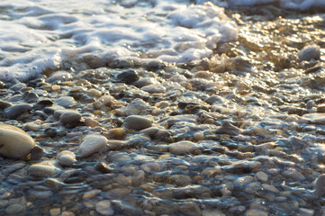 pebble stones on the sea beach, the rolling waves of the sea with foam
