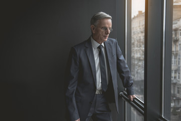 Portrait of pensive senior male looking at window while situating in room. Relax and labor concept