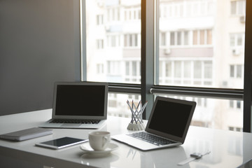 Fototapeta premium Two displays of modern notebook computers, cup of tea and copybook with electronic tablet situating on white table in office. Technology and interior concept