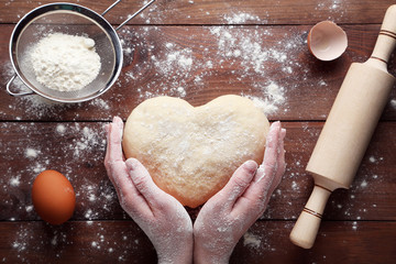 Female hands holding raw dough in heart shape on wooden table