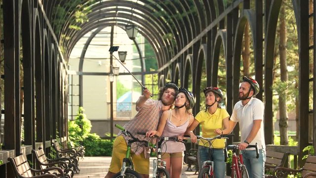 Young people having fun and taking selfie. Young funny cyclists posing and taking picture with monopod in park. Happy cheerful friends.
