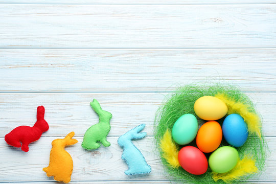 Colorful easter eggs in green nest with fabric rabbits on wooden table