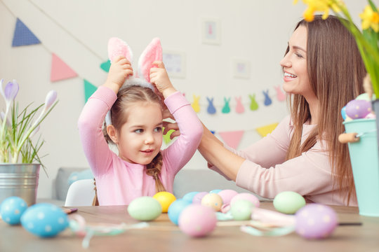 Mother and daughter in bunny ears easter celebration together at home sitting girl touching bazel