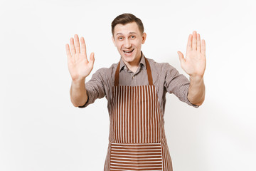 Fototapeta premium Young smiling man chef or waiter in striped brown apron, shirt showing palms to camera isolated on white background. Male housekeeper or houseworker. Domestic worker with copy space for advertisement.