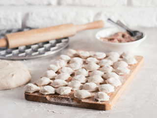 Uncooked russian pelmeni on cutting board and ingredients for homemade pelmeni on white table. Process of making pelmeni, ravioli or dumplings with meat. Copy space