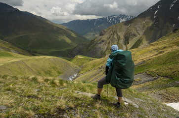 Backpacker girl on the mountain trail looks down to the valley. Epic view to Caucasus mountains at Tusheti (Georgia). Concept of travel lifestyle photo. 
