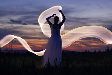 Woman in white dress dancing at sunset, light painting