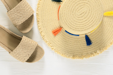 Womens summer accessories (straw hat and sandals) on white wooden background with copy space. Fashion beach travel concept. Flat lay