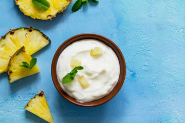 Homemade healthy breakfast. Greek yogurt in a bowl with pieces fresh pineapple on blue stone or...
