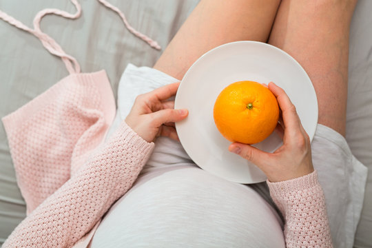 Pregnant woman eating orange. Aerial close up view.