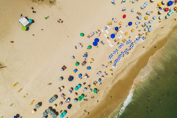 Aerial top view of people relaxing on the beach with ocean and colorful umbrellas