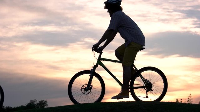 Young people riding bicycles at sunset. Company of young friends cycling against beautiful sunset. Amazing trip on bikes.