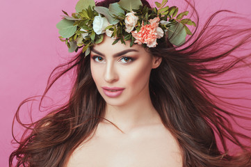 Naklejka premium Portrait of beautiful young sexual sensual woman with perfect skin make up streaming hair and flowers on head on pink background. Wreath of flowers Spring Summer Fashion Lifestyle People concepts.