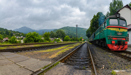 The old green locomotive stands at the railway station. In mountainous terrain