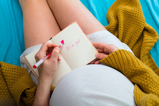 Pregnant woman writing in notebook. Aerial close up view.