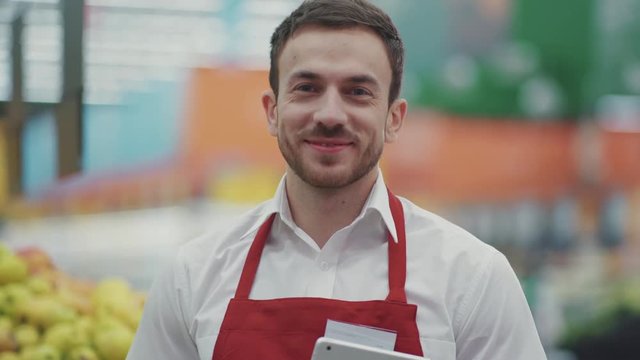 Close up face seller man in supermarket look camera smile vegetable business beautiful fresh produce retail shop worker food choosing young grocery healthy mall model shopping product portrait