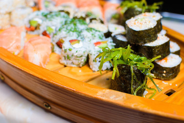 many kinds of sushi on a wooden stand in the form of a ship