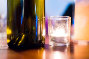 Macro closeup ground surface level view of bright white small candle light in restaurant wooden table by green glass wine bottle settting romantic dark atmosphere mood