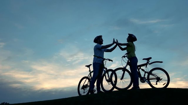 Couple of cyclists clapping hands together. Young man and woman having fun on bicycles at sunset. Best romantic rest together.