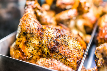 Macro closeup of roasted whole chicken brown with herbs, spices, crispy golden skin on tray in deli store shop grocery display