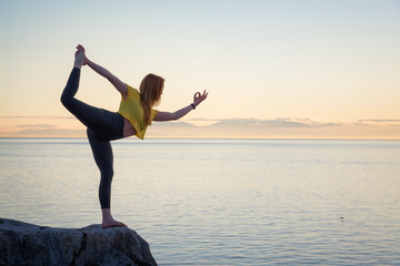 Young girl is practicing yoga during a vibrant sunset. Taken in Whytecliff park, Horseshoe Bay, Vancouver, BC, Canada.