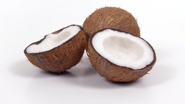 One whole ripe brown tropical coconut and two halves with yummy white pulp rotating on white isolated background. Healthy fresh tropical fruits. Loopable seamless cocos rotating