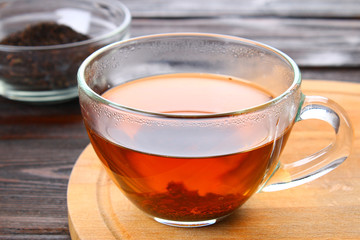 Hot black tea in a glass cup and dry tea on a wooden table.