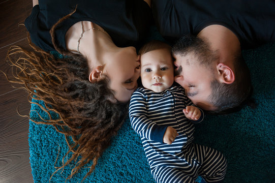 Father and mother kiss their son, lying on the floor in the house
