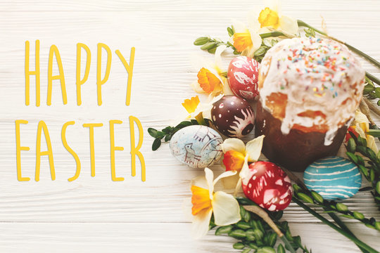 happy easter text. season's greetings card. happy Easter concept. stylish painted eggs and easter cake on white rustic wooden background with spring flowers. modern easter image