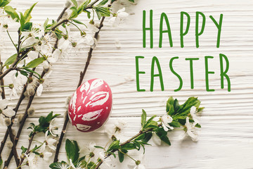 happy easter text. season's greetings card. stylish Easter flat lay. painted egg on rustic wooden background with spring flowers and willow branches.  modern colorful easter eggs