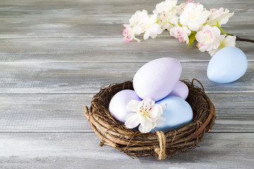 Hand-painted Easter eggs in a nest with spring flowers on a wooden gray background. Happy Easter