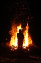 Silhouette of man by the fire at night. Man standing in front of bonfire. Flame on the ground.