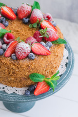 Homemade honey cake with strawberries, blueberries and raspberries on light background
