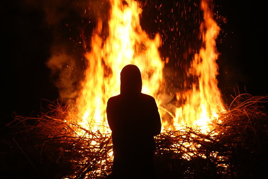 Silhouette Of Man By The Fire At Night. Man Standing In Front Of Bonfire. Flame On The Ground.