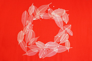 round frame of white skeletonized ficus leaves on a red background of corrugated paper.
