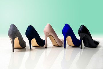 Different colors of high heels isolated green pastel background. Perfect high heels footwear, gray, navy blue, beige, blue, black. Matt and shiny high heels. Fashion and beauty. Female shoes.