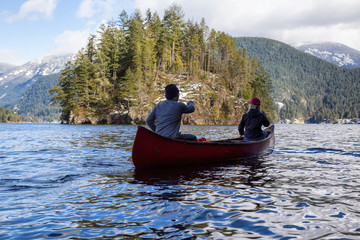 Couple friends on a wooden canoe are paddling in an inlet surrounded by Canadian mountains. Taken...