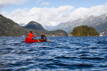 Couple friends on a wooden canoe are paddling in an inlet surrounded by Canadian mountains. Taken in Indian Arm, near Deep Cove, North Vancouver, British Columbia, Canada.