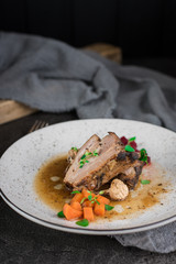 Pork ribs with beets, carrots, fried mushrooms and sauce on a white plate. Restaurant serving. Old black rustic background. Top view