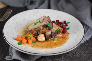 Pork ribs with beets, carrots, fried mushrooms and sauce on a white plate. Restaurant serving. Old black rustic background. Top view