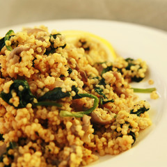 Millet with mushrooms and spinach. Jewish cuisine. Vegetarian couscous on the round white plate. Close up. Toned photo.