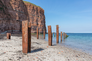 Beach Helgoland island with red cliffs and rusty iron pillars of old putrefied jetty