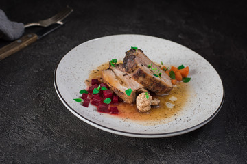 Pork ribs with beets, carrots, fried mushrooms and sauce on a white plate. Restaurant serving. Old black rustic background. Top view