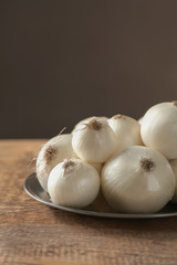 Plate with ripe onions on wooden table