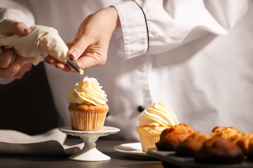 Chef decorating tasty cupcake with cream at table